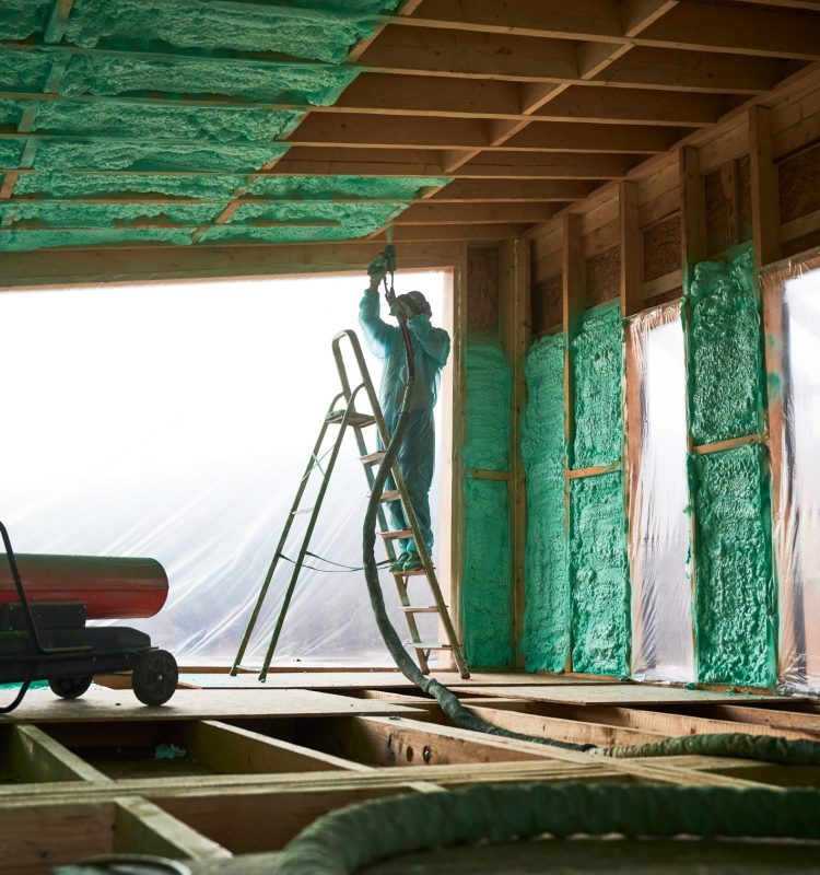 Male builder insulating wooden frame house. Man worker spraying polyurethane foam inside of future cottage, standing on ladder, using plural component gun. Construction and insulation concept.
